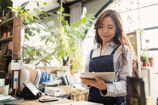 A local small business owner in Canton, Ohio, wearing an apron, happily manages operations on a tablet. This highlights CCW's POS and local IT support services for businesses and residents.